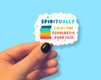 May include: A white sticker with a colorful stack of books and the text "Spiritually I'm at the Scholastic Book Fair."