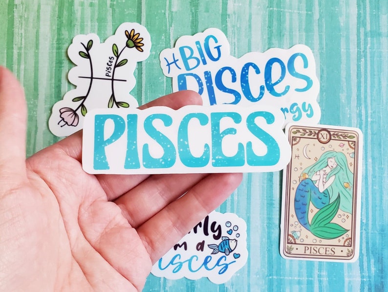 May include: A set of five stickers featuring the zodiac sign Pisces. The stickers are white with blue and green accents. One sticker features the Pisces symbol, another says "Big Pisces Energy", another says "Pisces", another says "I'm a Pisces", and the last one is a tarot card with a mermaid and the word "Pisces".