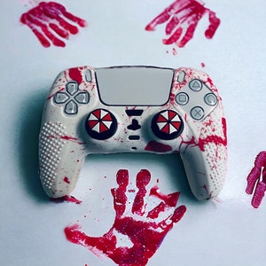 May include: A white video game controller with red splatter paint design. The controller has two round buttons with black and white umbrella designs.