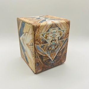 May include: A brown and gold card deck box with a geometric design featuring a central triangle with a sword and eye motif.