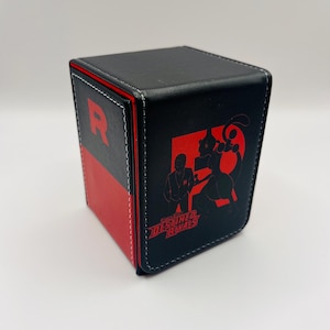 May include: Black and red cube-shaped card storage box. The box features a red "R" on one side and a graphic of a character and text from "Destined Rivals" on another. White stitching accents the edges.