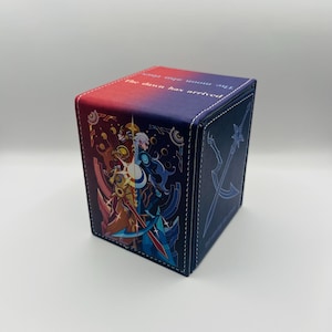 May include: A rectangular deck box with a red and blue gradient top featuring the text The dawn has arrived. The front panel displays a split illustration of a character in gold and blue armor, while the side panel shows a blue sword graphic.