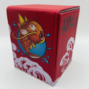 May include: Red deck box with a cartoon illustration of a red and orange fish with a crown on its head. The fish is surrounded by white clouds and blue water droplets. The text "波乗り" is on the side of the box.