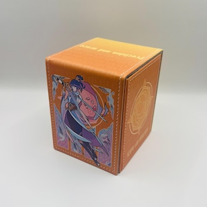 May include: A rectangular orange deck box featuring a graphic illustration of a character holding a staff on the front panel. The top edge displays the text "precision and grace" in white, while the side panel shows a circular emblem design.