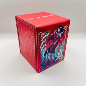 May include: Red card storage box with a detailed illustration of a character with long black hair and a red and black outfit. The box has white stitching and the words "SHALL NOT FALL" printed on the top.