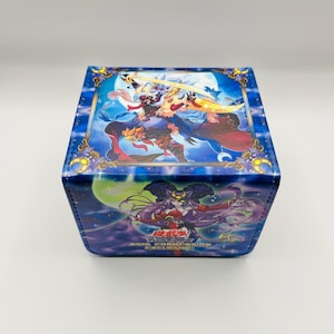 May include: A blue, square card storage box with colorful anime-style illustrations. The top panel features a character with a sword, while the side panel displays a purple-haired character. The box has a starry night sky background.