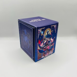 May include: A square, blue card storage box with white stitching. The box features a colorful illustration of a figure with a sword and a crescent moon. The text "Man The Barricades" is printed on the top.