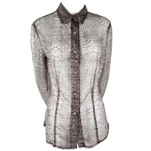 May include: A long-sleeved button-down shirt featuring a semi-sheer fabric with a grey and brown snakeskin print. The garment includes a pointed collar, a central button placket with visible buttons, and vertical seam detailing along the front.