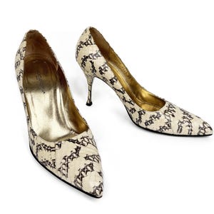 Può includere: Un paio di décolleté con tacco alto con motivo a pelle di serpente color crema e nero. Le scarpe hanno la punta a punta, tacchi a spillo e solette dorate. I tacchi sono alti circa 7,6 cm.