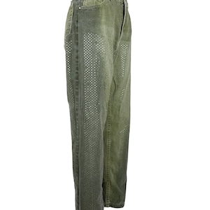 Op de afbeelding: Olijfgroene denim jeans met een rechte pijp. De jeans hebben een patroon van kleine, vierkante uitsparingen aan de voorkant van elke broekspijp. Ze hebben een klassiek ontwerp met vijf zakken en een knoop- en ritssluiting.