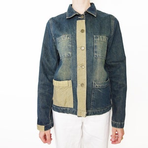 Peut inclure: Une veste en jean bleu avec une poche plaquée marron sur le devant. La veste a une fermeture à boutons et des manches longues.