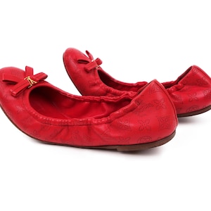 May include: A pair of red leather ballet flats with a gold bow detail. The flats have a subtle embossed pattern.