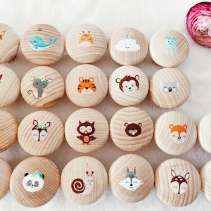 Peut inclure: Vingt-quatre cercles en bois avec des motifs d'animaux et de la nature peints. Chaque cercle présente un motif différent, notamment un renard, une baleine, une girafe, un nuage, une méduse, un écureuil, une souris, un tigre, un singe, un koala, un pingouin, un cerf, un hibou, un ours, un escargot, un loup, un cerf et une souris. Les cercles sont disposés en grille sur une surface blanche.