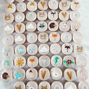 Op de afbeelding: Een set van 48 houten cirkels met verschillende geschilderde ontwerpen, waaronder dieren, harten, wolken, regenbogen en een luchtballon. De cirkels zijn ongeveer 5 cm in diameter en hebben een natuurlijke houten afwerking.