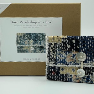 May include: A brown box with the text "Mindful Stitch Kit" and "Boro Workshop in a Box" on the front. The box contains a kit to hand stitch a small boro inspired pouch. The pouch is made of blue and white fabric with a floral pattern and has two white buttons.
