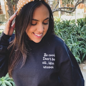 Puede incluir: Una sudadera negra con el texto "Be cool Don't be all, like, uncool" en letras blancas.