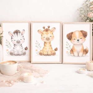 Könnte beinhalten: Drei gerahmte Aquarelldrucke mit entzückenden Babytieren: einem Zebra, einer Giraffe und einem Welpen. Jedes Tier ist in sitzender Position mit einem lächelnden Gesichtsausdruck dargestellt, umgeben von weichen Pastellfarben und botanischen Akzenten. Die Rahmen sind aus hellem Holz.