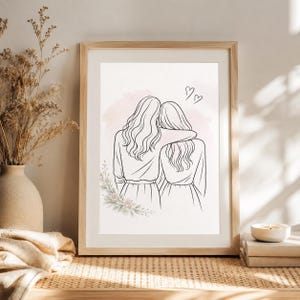 Könnte beinhalten: Ein gerahmter Kunstdruck mit Strichzeichnung von zwei Personen mit langem Haar, die nebeneinander stehen, wobei eine den Arm um die andere legt. Die Illustration enthält einen zarten rosa Aquarellhintergrund, ein kleines Blumenmotiv unten links und zwei Herzen.