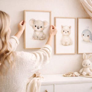 Könnte beinhalten: Drei gerahmte Aquarelldrucke mit niedlichen Babytieren: einem Koala, einem flauschigen weißen Lamm und einem lächelnden blauen Wal. Die hellen Holzrahmen schaffen eine weiche, neutrale Ästhetik, ideal für ein Kinderzimmer, mit Pastellfarben.