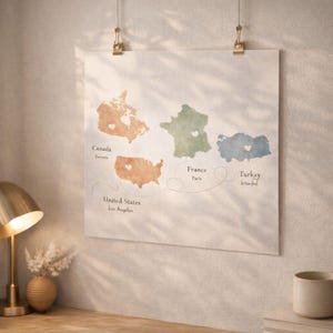 Könnte beinhalten: Ein Aquarell-Weltkarten-Druck mit Kanada, den Vereinigten Staaten, Frankreich und der Türkei, jeweils in einer anderen Farbe. Die Städte Toronto, Los Angeles, Paris und Istanbul sind beschriftet. Der Druck wird von zwei goldenen Clips gehalten.