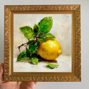 May include: A framed oil painting of a lemon with green leaves. The lemon is a vibrant yellow, and the leaves are a lush green. The painting is in a gold ornate frame, adding a touch of elegance to the artwork.