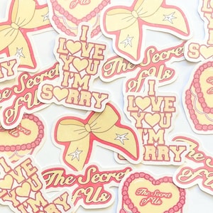 May include: A collection of pink and yellow stickers featuring various designs, including hearts, bows, and text. The text on the stickers includes "I love you I'm sorry", "The Secret of Us", and "The Secret of Us".