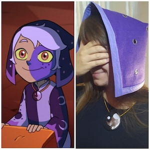 May include: A purple hooded cowl with silver eyelets and a matching pendant necklace. The necklace features a black pendant with a moon and star design. The image also shows a cartoon character with a similar outfit.