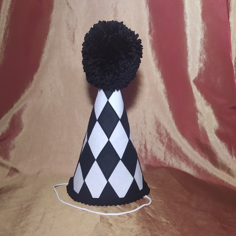 May include: A black and white checkered party hat with a black pom-pom on top.