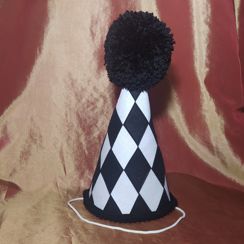 May include: A black and white checkered party hat with a black pom-pom on top. The hat has a white string attached to the bottom.