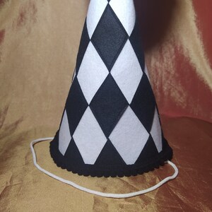 May include: A black and white checkered party hat with a white string attached. The hat has a black trim around the bottom edge.