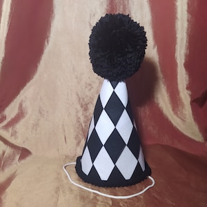 May include: A black and white checkered party hat with a black pom-pom on top. The hat has a white elastic band.
