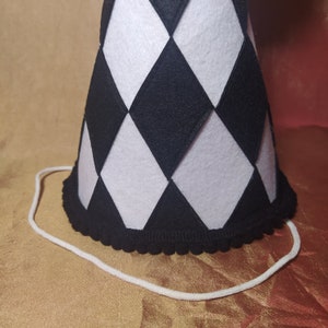 May include: A black and white checkered party hat with a black pom-pom trim and a white string attached.