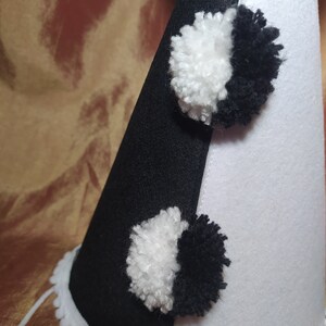 May include: A black and white felt party hat with two pom-poms. The hat is divided diagonally, with one side black and the other white. The pom-poms are half black and half white. The hat has a white scalloped trim.