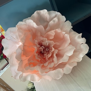 May include: A large, artificial peony flower in peach and cream hues. The layered petals have a textured appearance, with a darker centre. This flower is likely for decorative purposes or crafting.