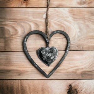 May include: A black metal heart-shaped frame with a smaller metal heart hanging inside. The smaller heart has a floral design.