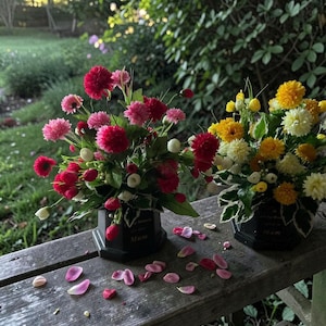 May include: Two floral arrangements in black vases, one with red and pink flowers, the other with yellow and white blooms. The vases are inscribed with the word "Mum". Pink and red petals are scattered on the wooden surface.
