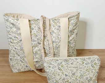 May include: A quilted tote bag and a matching zippered pouch, both featuring a cream-colored fabric with a small-scale floral print in blue, green, and brown. The tote has wide cream webbing straps and the pouch displays a label reading ArtiTextures.