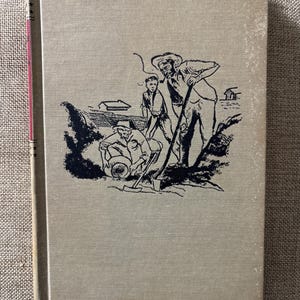 May include: A vintage book with a beige cover and a black and white illustration of three men working outdoors. The spine is red. The illustration depicts a man with a shovel, another with a bucket, and a third standing nearby.