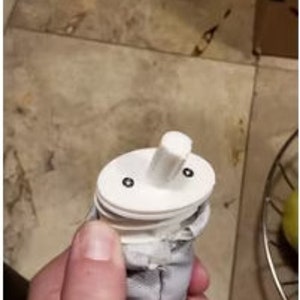 Op de afbeelding: Witte plastic filter met twee kleine zwarte schroeven aan de bovenkant. De filter is bevestigd aan een grijze stoffen buis.