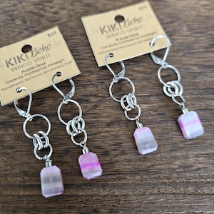 May include: Three pairs of earrings with purple opal stones and silver-colored metal chains. Each earring has a rectangular purple and white stone, connected by multiple chain links. The earrings are labeled "KIKI Boho Indigo Spirit Purple Opal".
