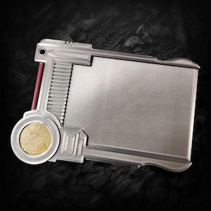 Könnte beinhalten: Ein silberfarbener Kartenhalter aus Metall mit einem runden, goldfarbenen Akzent auf der linken Seite. Der Kartenhalter hat eine strukturierte Oberfläche und einen roten Streifen auf der linken Seite.