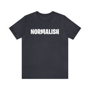 以下が含まれることがあります： 前面に白い文字で「NORMALISH」とプリントされた濃い青色のTシャツです。