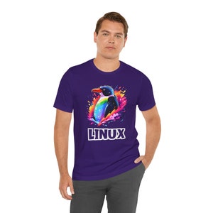 Pode incluir: Uma camiseta roxa com um gráfico de pinguim colorido e a palavra "LINUX" em letras brancas.