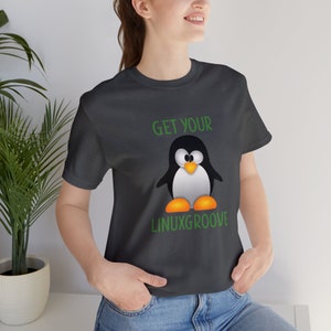 Puede incluir: Una camiseta negra con un gráfico verde de un pingüino de dibujos animados y el texto "GET YOUR LINUXGROOVE".