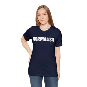 以下が含まれることがあります： 前面に白い文字で「NORMALISH」とプリントされたネイビーブルーのTシャツです。