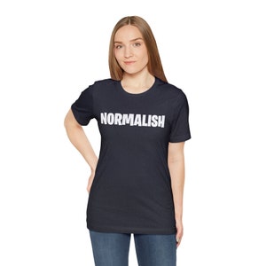以下が含まれることがあります： 前面に白い文字で「NORMALISH」がプリントされたネイビーブルーのTシャツです。