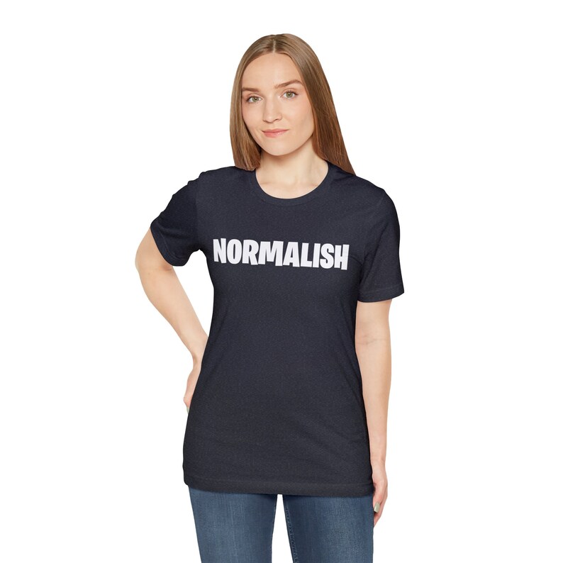 以下が含まれることがあります： 前面に白い文字で「NORMALISH」がプリントされたネイビーブルーのTシャツです。