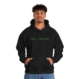 May include: Black hooded sweatshirt with a front pocket. The sweatshirt features the green text "2>&1 > /dev/null". The model is wearing blue jeans.