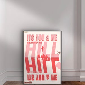 May include: A framed poster with a red and white design. The text "ITS YOU & ME" is at the top, with "BE RUNNING UP THAT HILL" below. The word "HILL" is prominently displayed, with figures and text reflected below. The bottom text reads "1100 & WE".