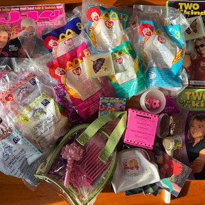 May include: A collection of vintage items, including magazines, McDonald's Happy Meal toys, and a clear cosmetic bag with pink accessories. The magazines feature celebrity covers. The toys are in sealed plastic packaging.